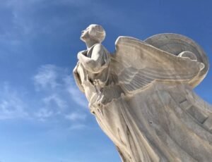 Stone angel statue viewed from below against a blue sky