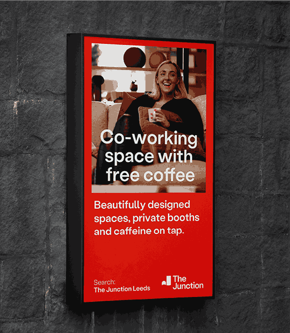 Digital advertising display promoting a co-working space, featuring a person holding a coffee and bold marketing text in a modern red visual design.